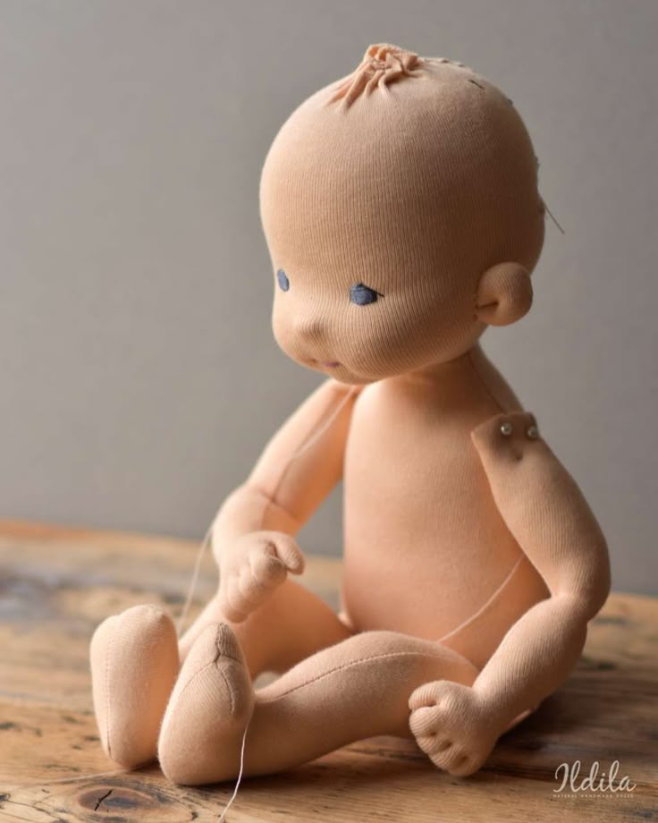 a stuffed baby doll sitting on top of a wooden table next to a thread spool