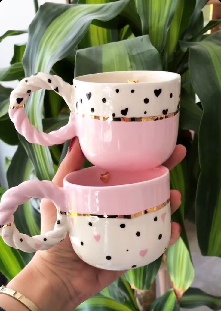 two pink coffee mugs with black hearts on them, one is holding the other