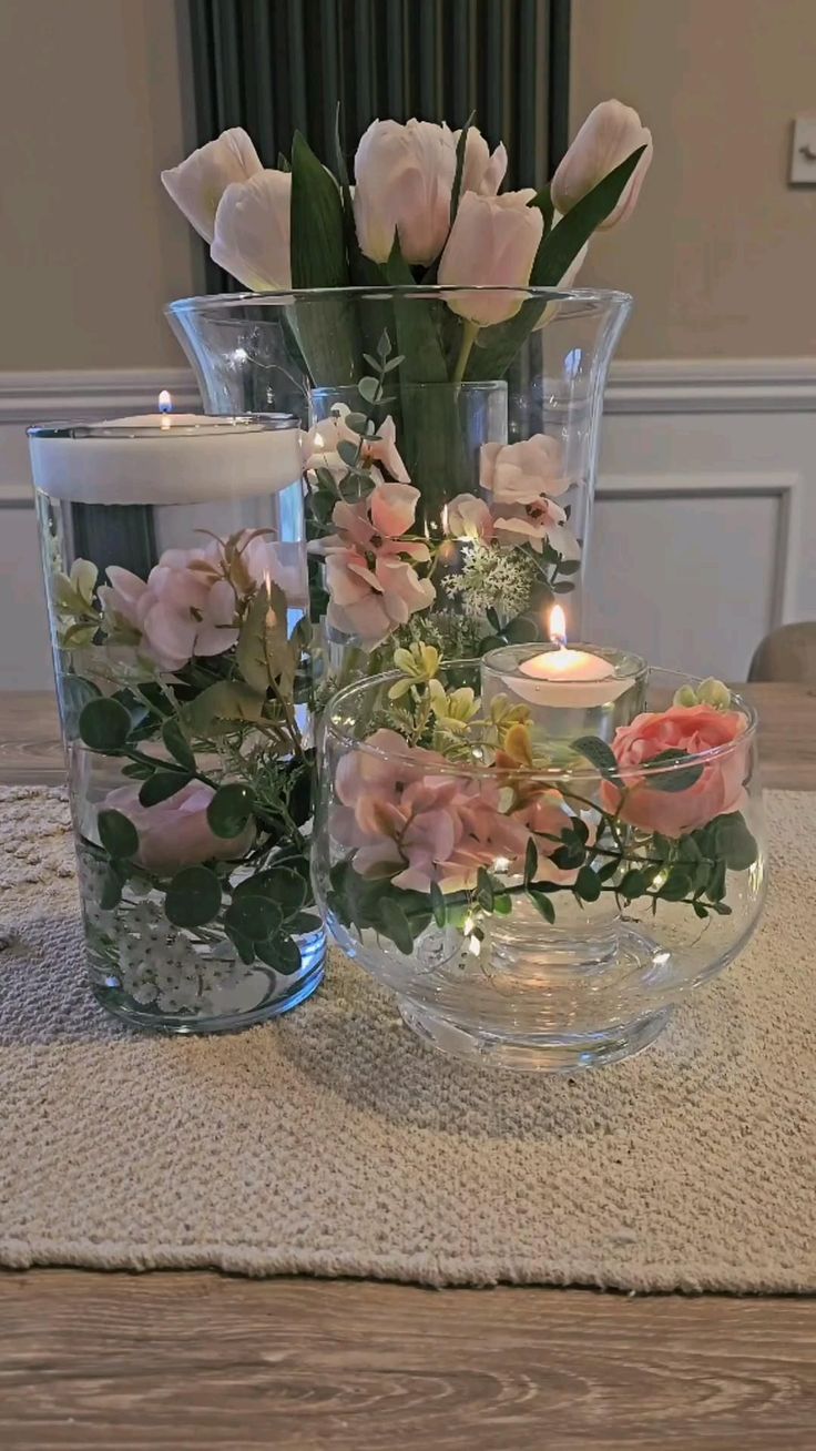 two vases filled with flowers on top of a wooden table next to a candle