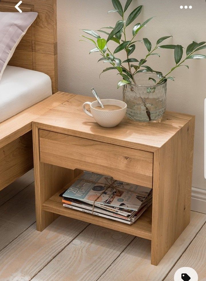 a small wooden table with a bowl on it next to a bed and plant in the corner