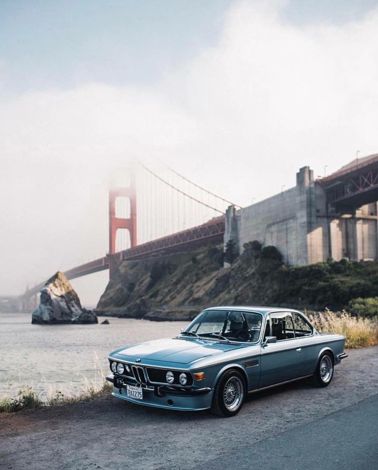 an old blue car parked in front of the golden gate bridge