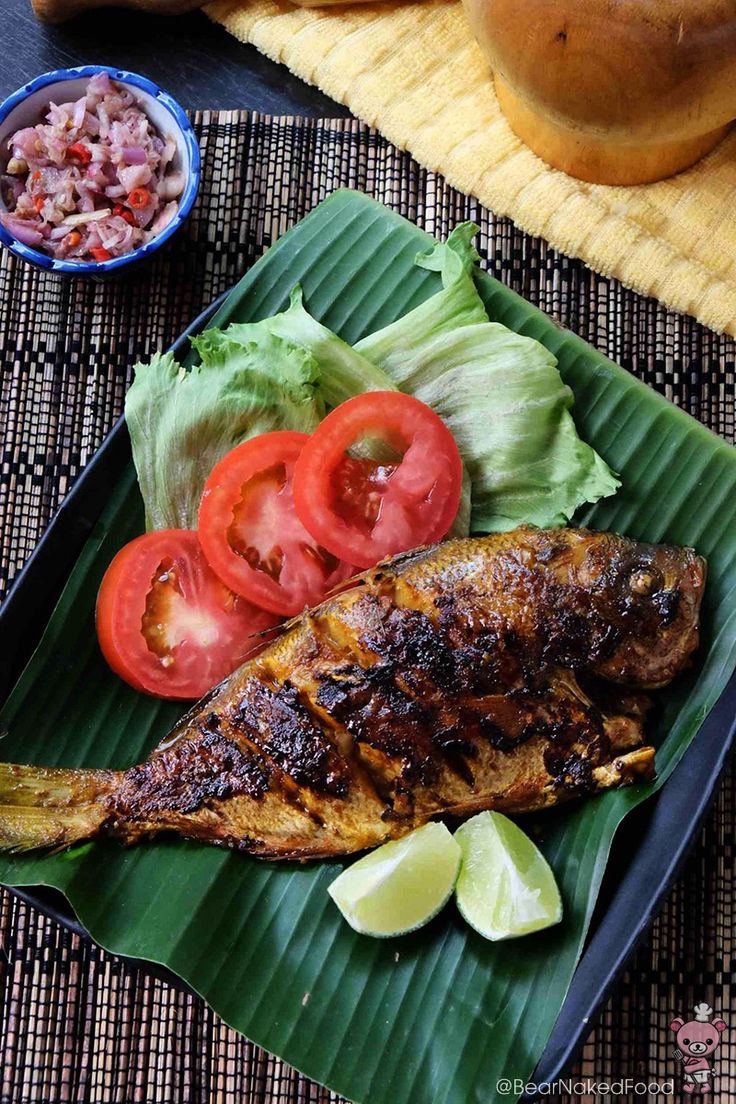 grilled fish and vegetables on a green leafy platter with sliced tomatoes, lettuce and lemon wedges