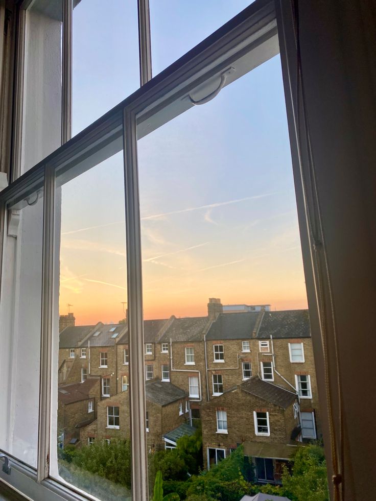 an open window with the view of houses and buildings outside at sunset or dawn in the city