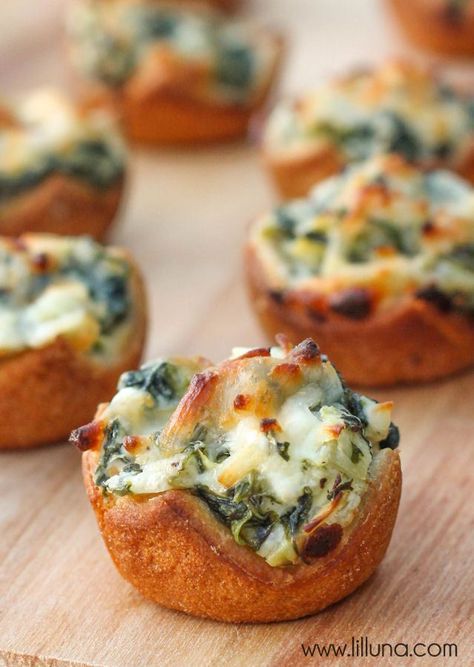 mini pizzas with spinach and cheese are on a wooden board, ready to be eaten