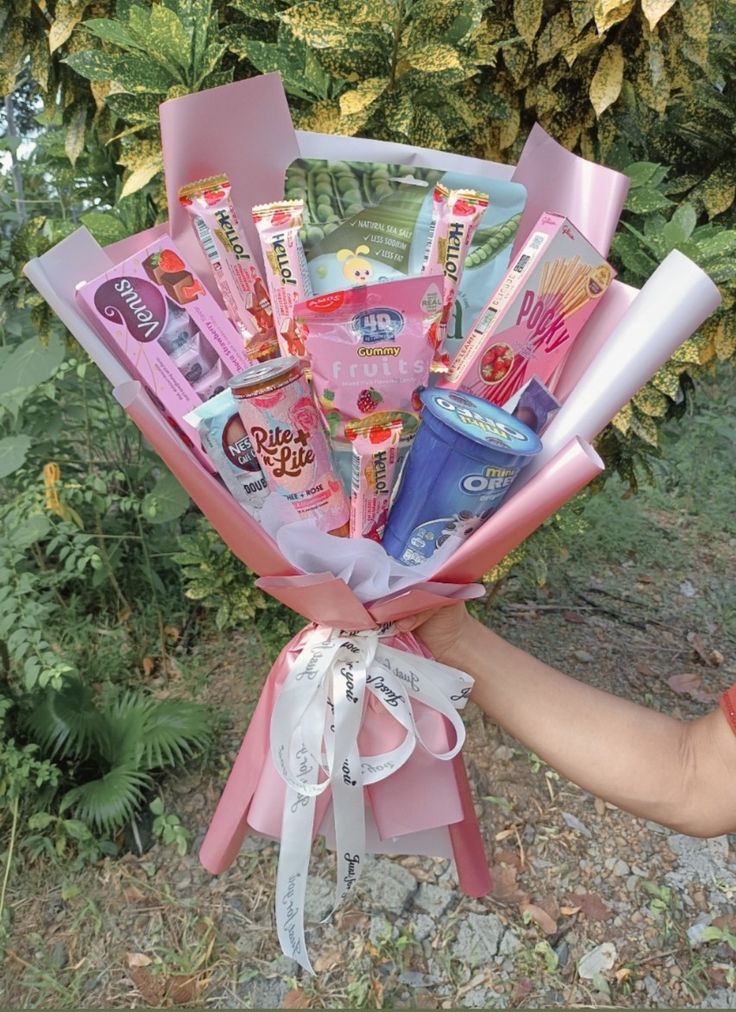 a person holding a bunch of candy and toothpaste wrapped in pink tissue paper