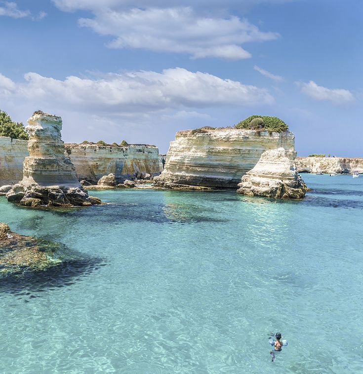 a person swimming in the clear blue water near some rocks and cliffs on an island