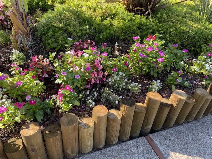 some flowers are growing on the side of a wooden fence in front of bushes and trees