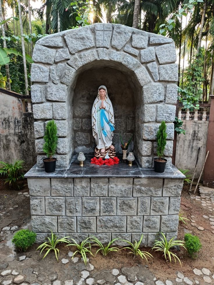 a statue of the virgin mary in front of a stone oven with potted plants