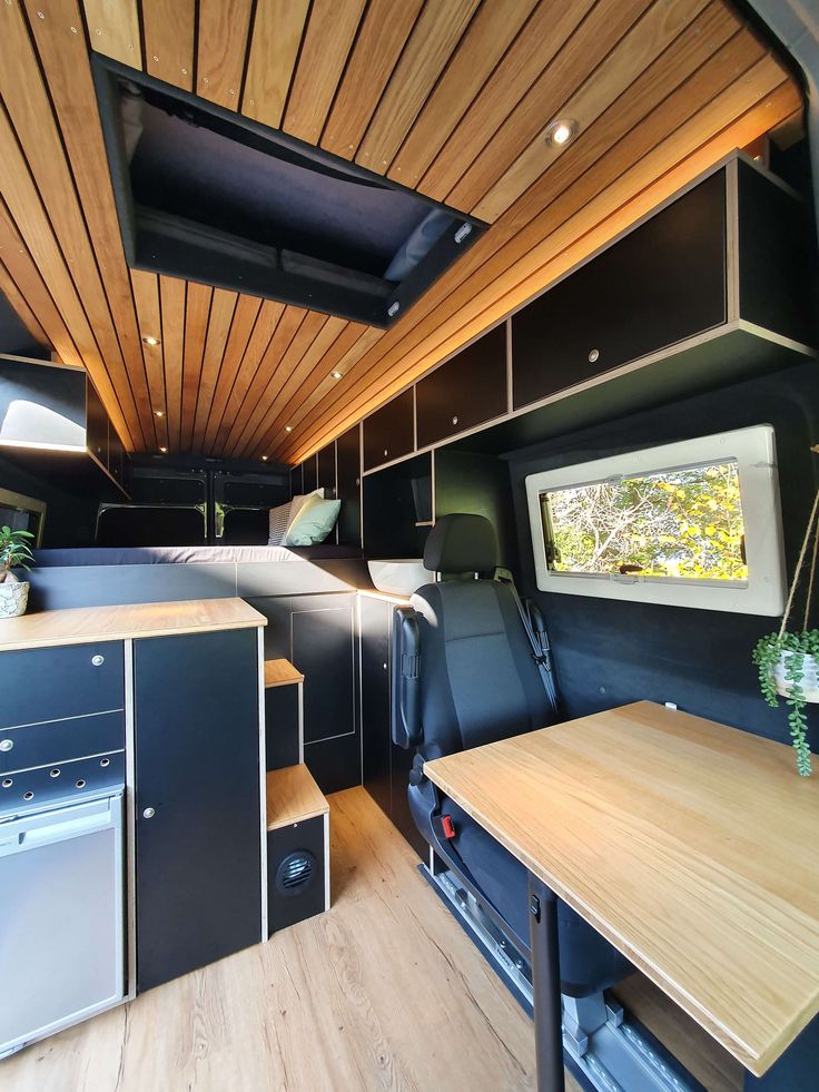 an interior view of a camper with wood paneling and black furniture, including a kitchenette