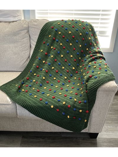 a green crocheted blanket sitting on top of a couch next to a window