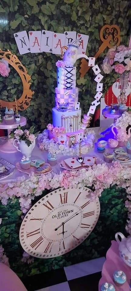 a table topped with lots of cake and cupcakes next to a wall covered in flowers