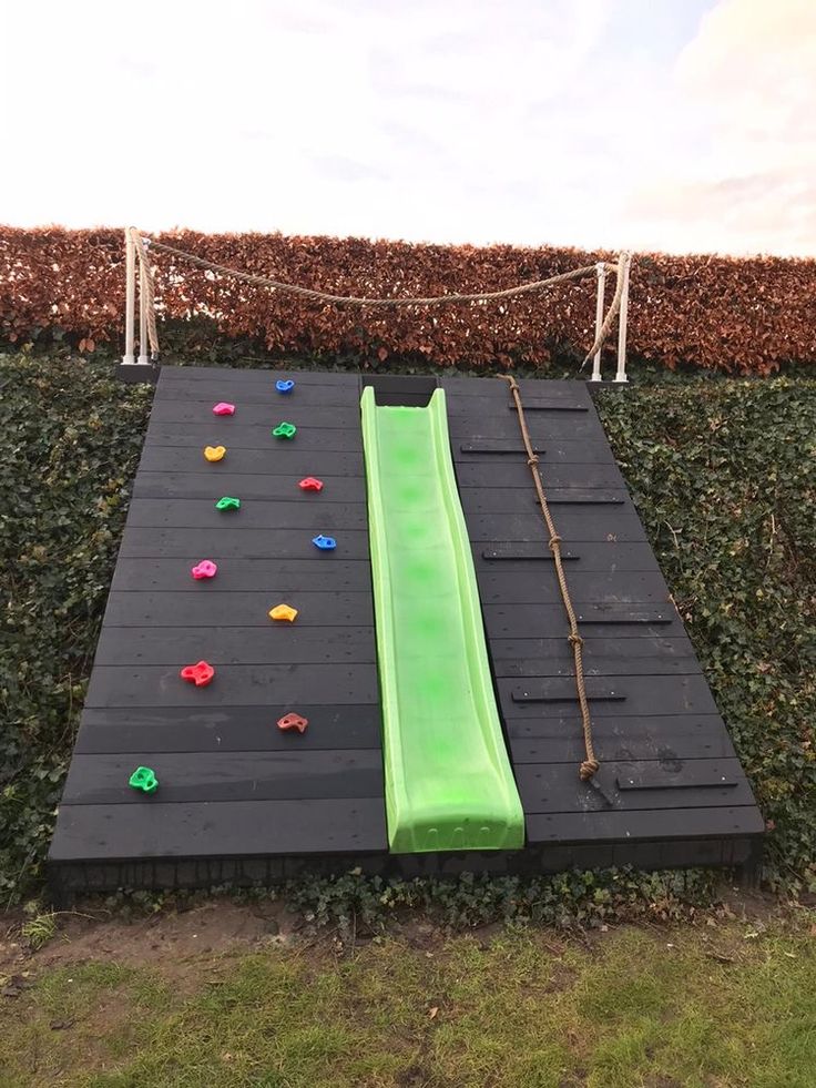 an inflatable slide is set up on the ground next to a hedge wall