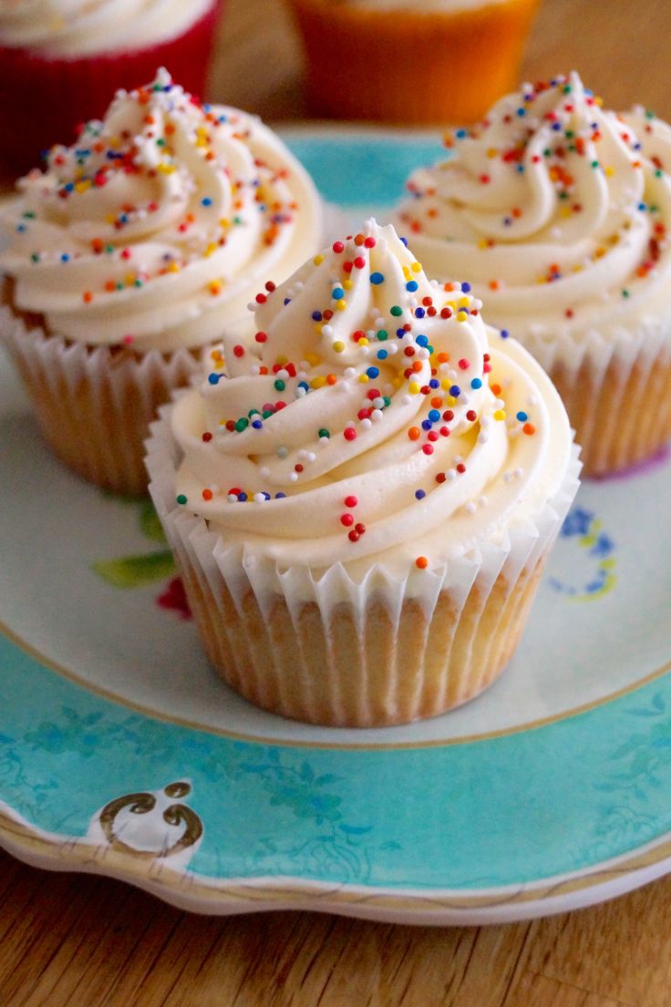 three cupcakes with white frosting and sprinkles on a plate