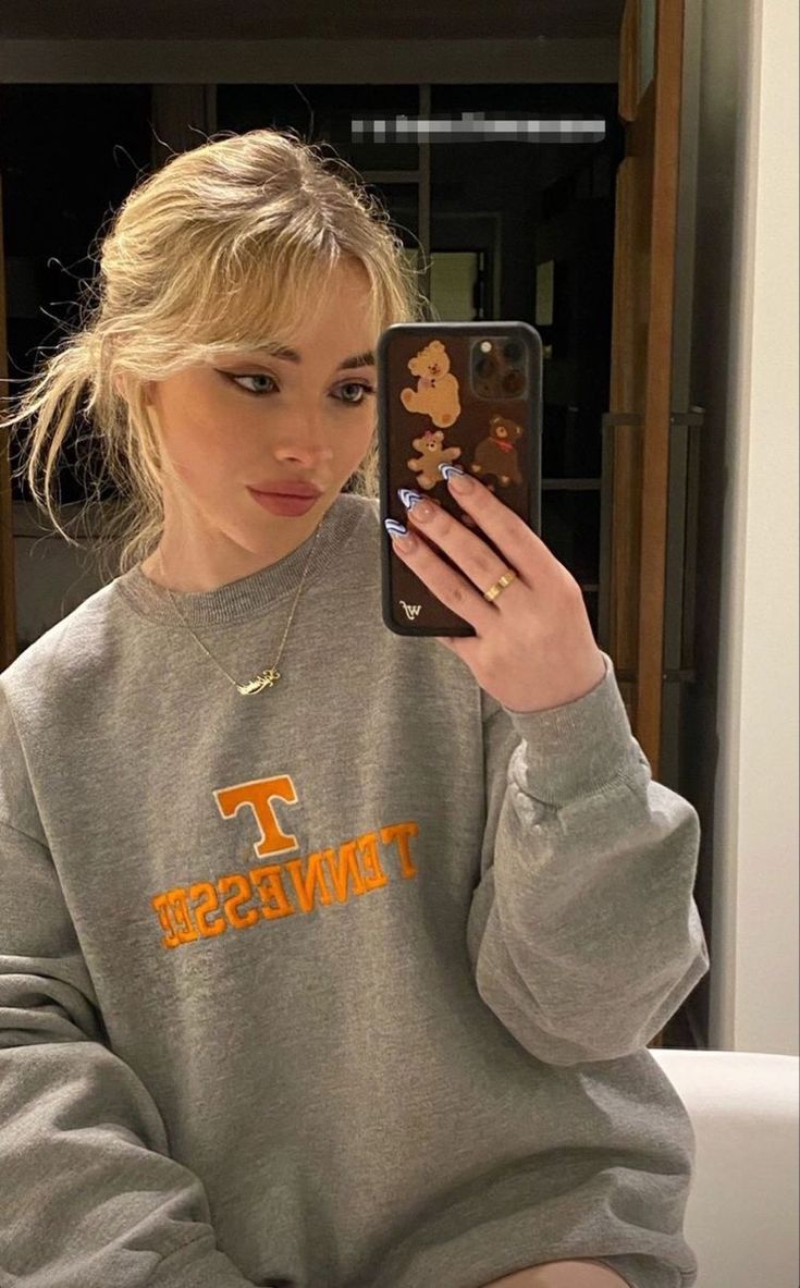 a woman is taking a selfie in front of her cell phone while wearing a sweatshirt