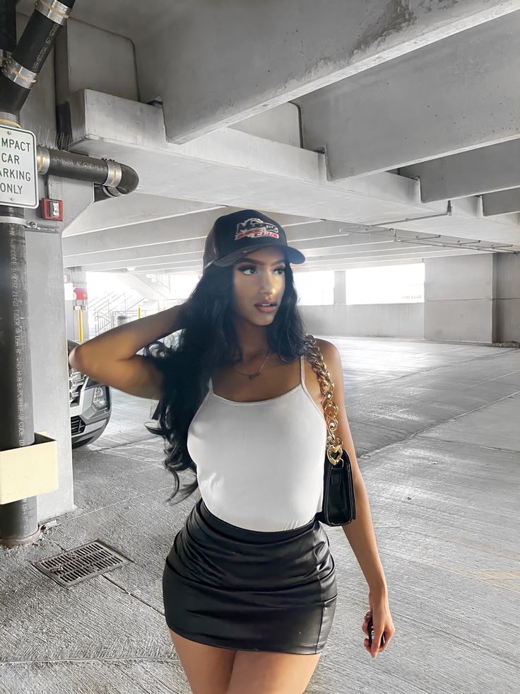 a woman in a white top and black skirt is standing under a parking garage with her hand on her hip