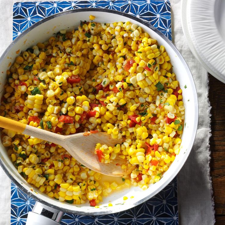 a pot filled with corn on top of a blue and white place mat next to a wooden spoon