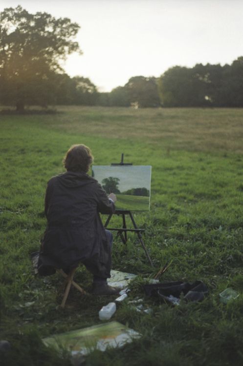 a person sitting in the grass painting on an easel