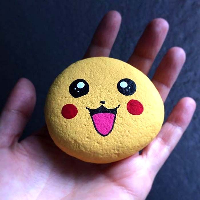 a hand holding a yellow rock with a smiley face painted on it