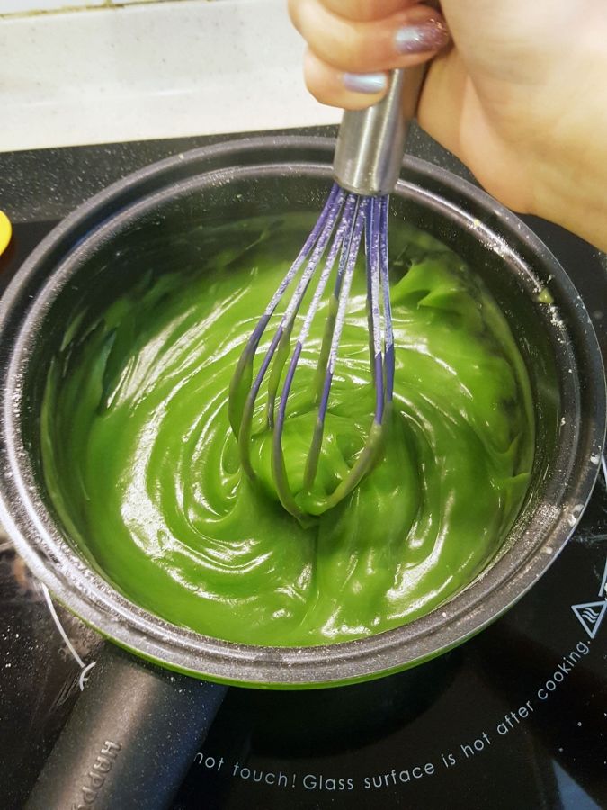 a person whisking green liquid into a metal bowl on top of a stove