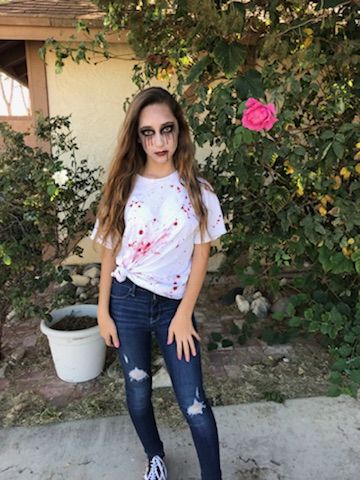 a young woman standing in front of a bush with blood on her shirt and jeans