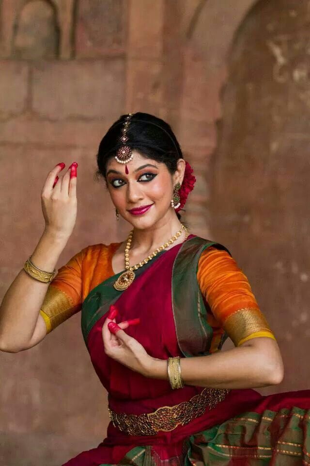 a woman in a red and green sari holding her hand up to her face