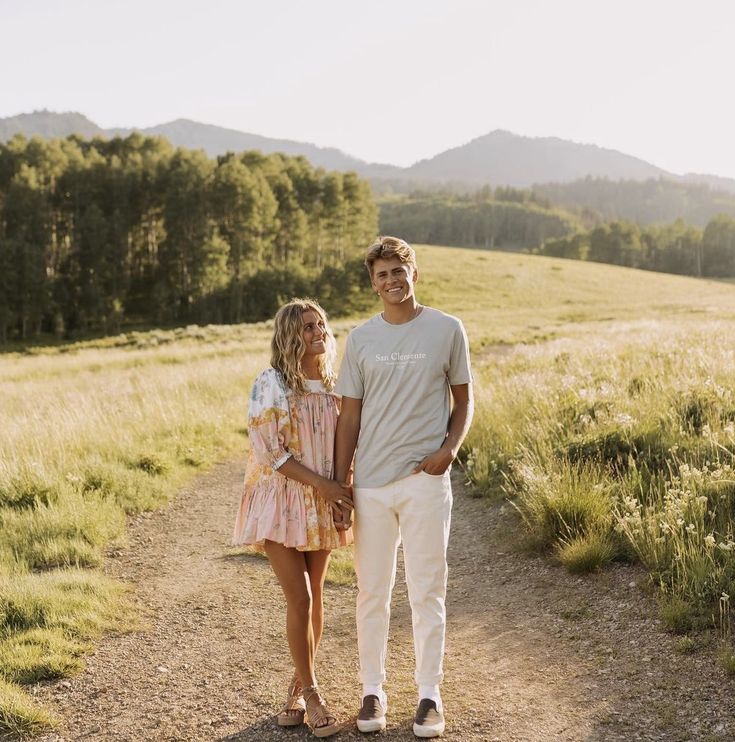 a young man and woman standing on a dirt road in the middle of a field