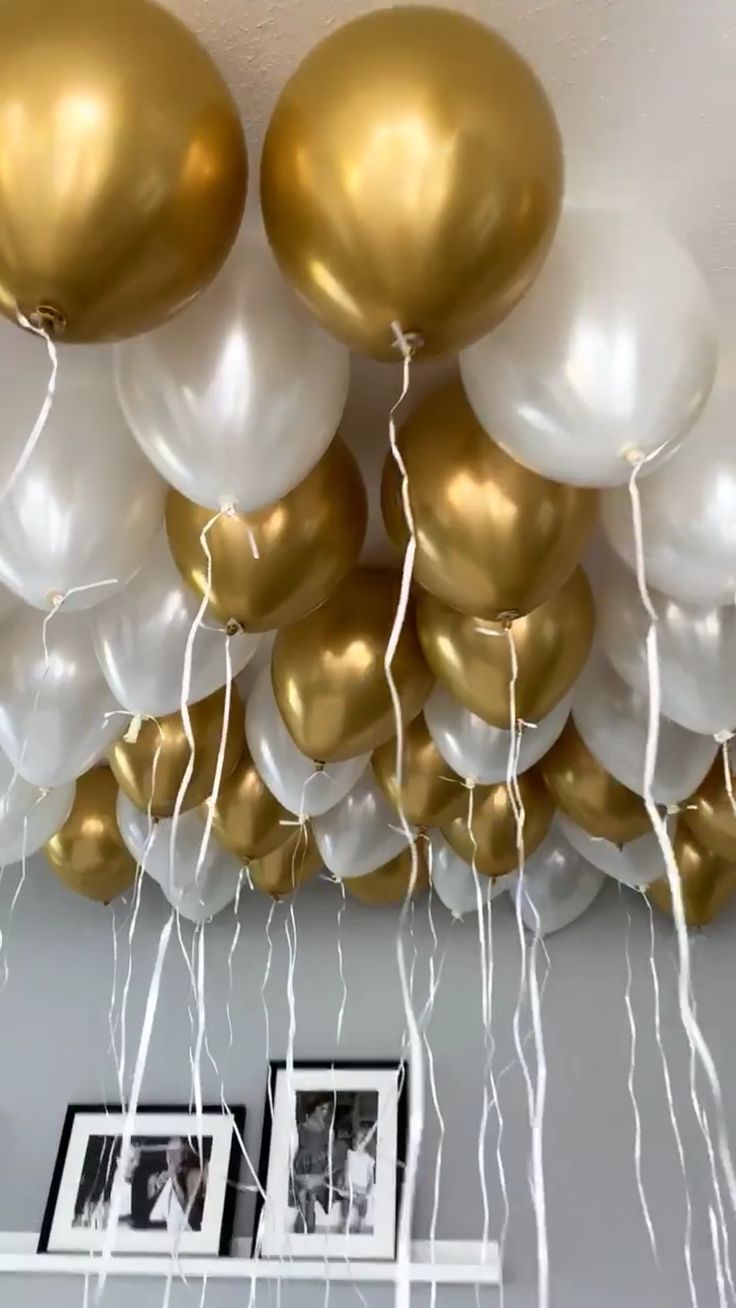 gold and white balloons are hanging from the ceiling in front of two pictures on a shelf