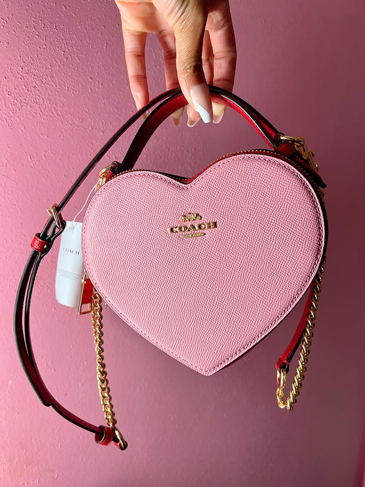 The Coach Heart Bag is the new it bag that recently dropped at the Coach Outlets. It's hard to find, but check out my blog to see how I was able to get one! Heart Coach Purse, Coach Bags Heart, Pink Coach Bag Aesthetic, Coach Valentine Bag, Coach Heart Bag Outfit, Heart Coach Bag, Coach Heart Purse, Pink Luxury Bag, Heart Bag Outfit