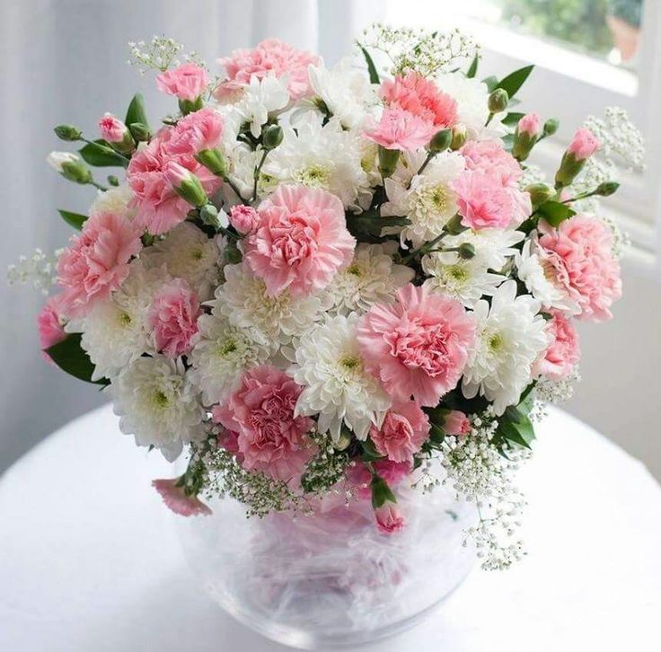 a vase filled with pink and white flowers on top of a table next to a window