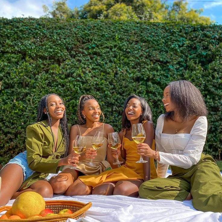 three women sitting on a blanket holding wine glasses