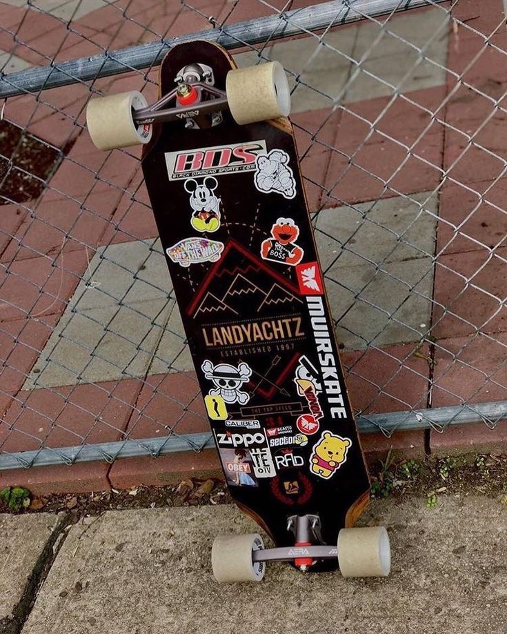 a skateboard with stickers on it leaning against a fence