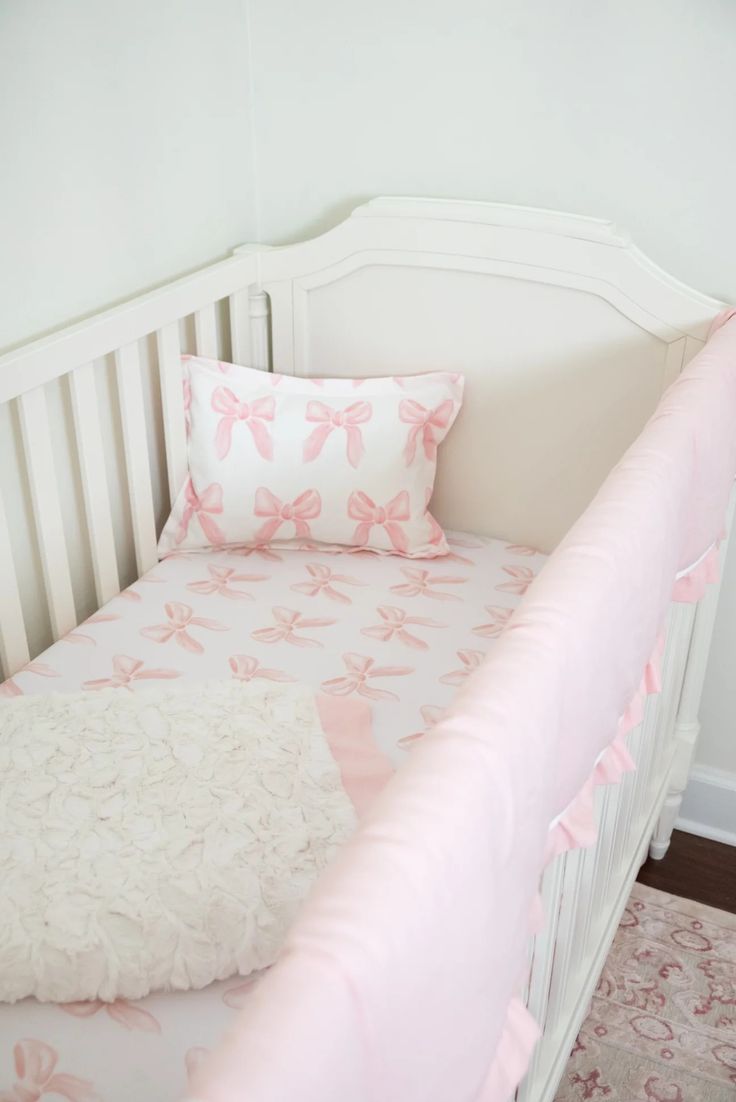 a white crib with pink and white bedding on it's bottom half