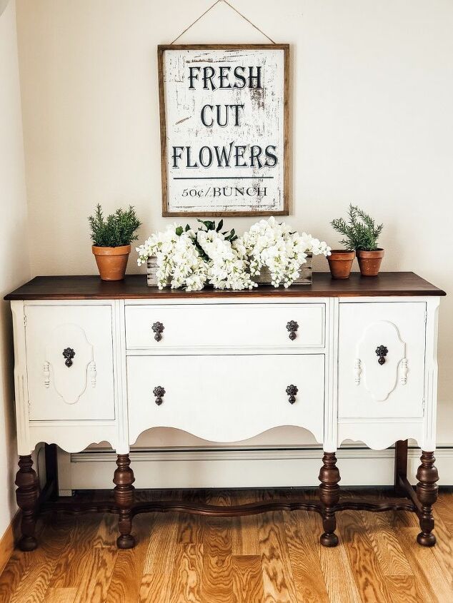 a white dresser with flowers on top and a sign above it