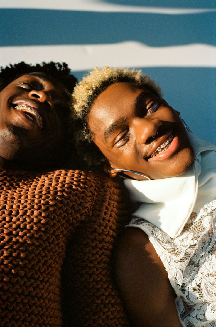 two men are laying down and smiling for the camera, one is wearing a brown sweater