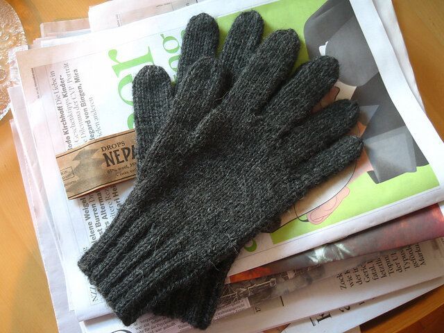 a pair of gray knitted gloves sitting on top of newspapers