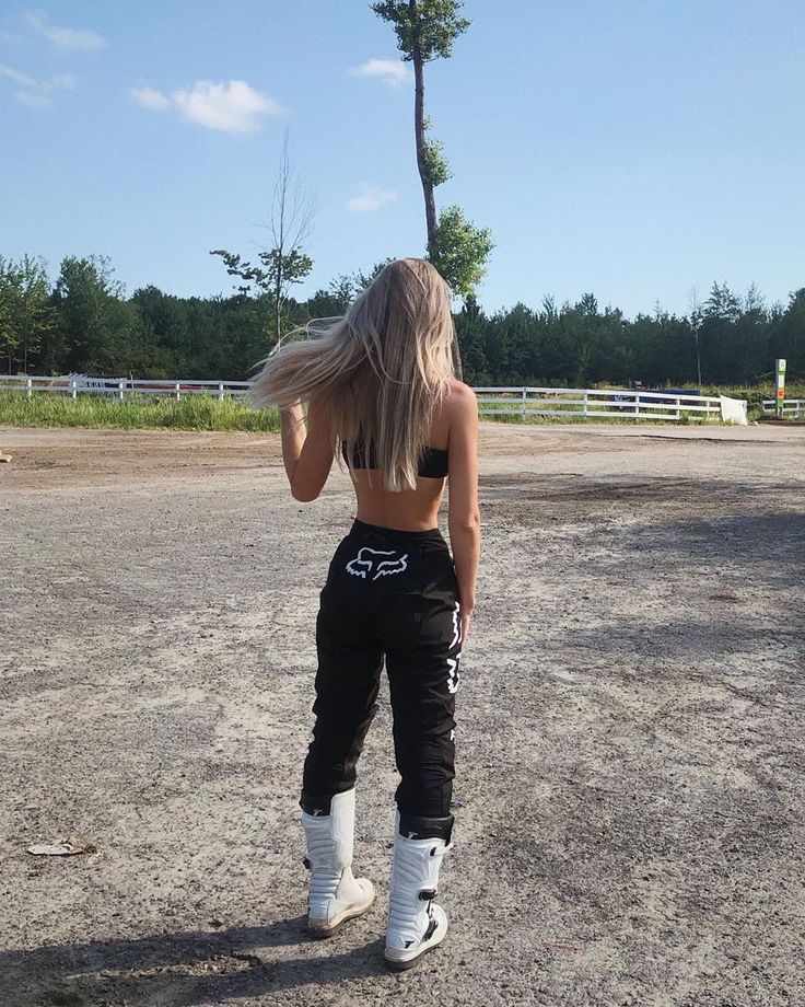 a woman standing in the dirt with her back to the camera, wearing black pants and white boots