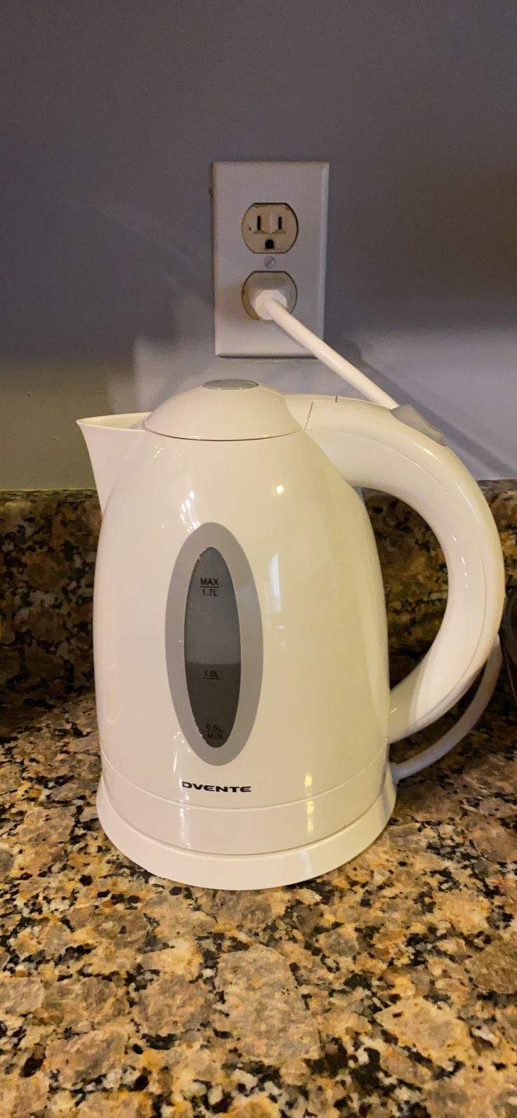 a white electric tea kettle sitting on top of a counter next to a light switch