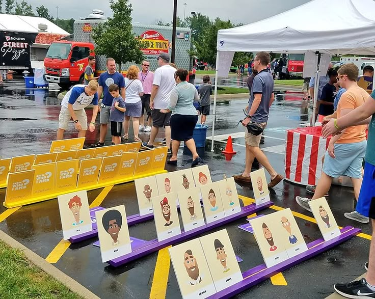 a group of people standing next to each other near tables with pictures on them in the rain