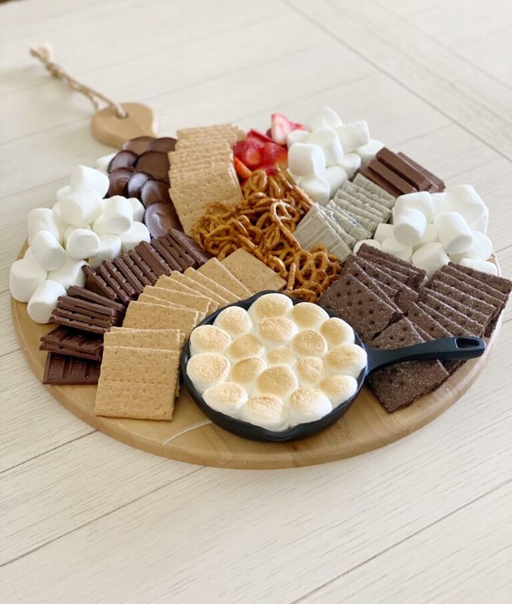 a wooden plate topped with marshmallows, graham crackers and other snacks