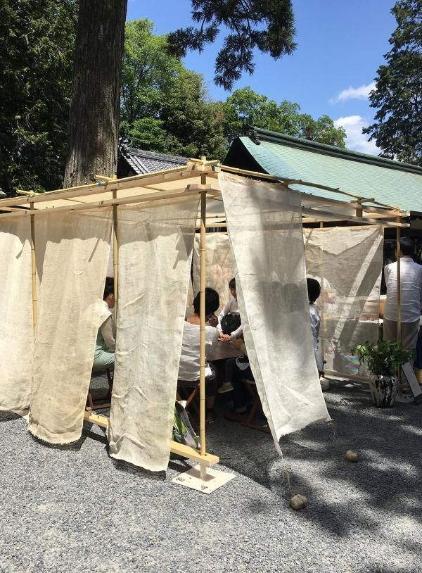 some people are sitting at a table under a tree with curtains on the outside wall