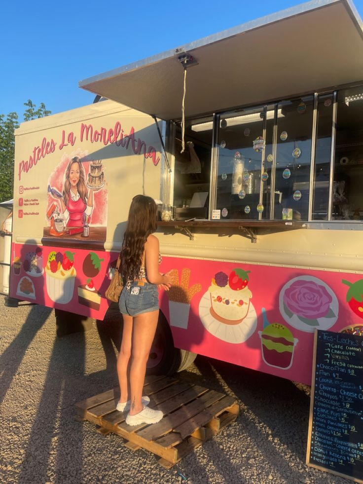 a woman standing in front of a pink and white truck with cupcakes on it