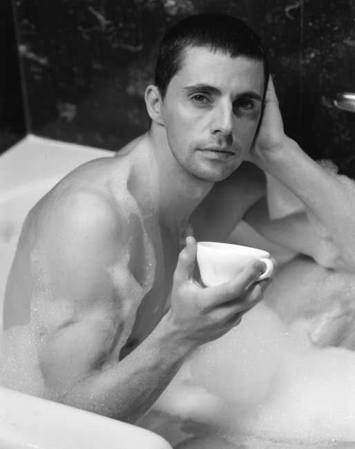 a shirtless man sitting in a bathtub holding a cup