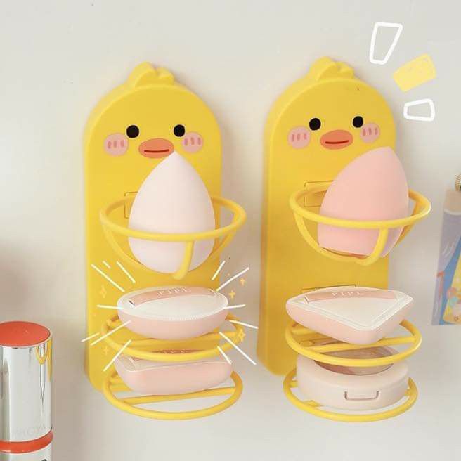 there are two yellow wall hooks with pink items on them and one is holding an egg