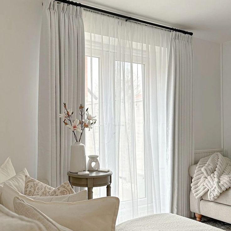 a bedroom with white walls and curtains on the windowsills is decorated in neutral tones