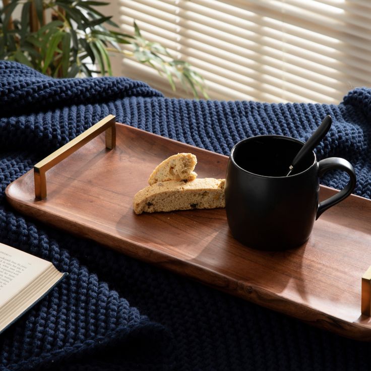 a tray that has some bread and a coffee cup on it with a book next to it