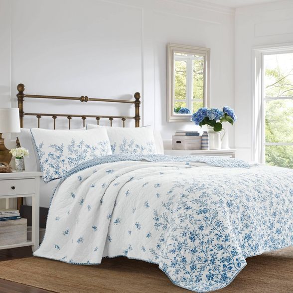 a bed with blue and white flowers on it in a bedroom next to a window