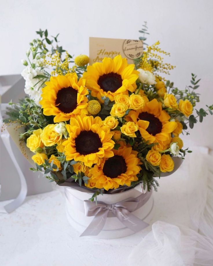 a bouquet of sunflowers in a white vase with a note on the side