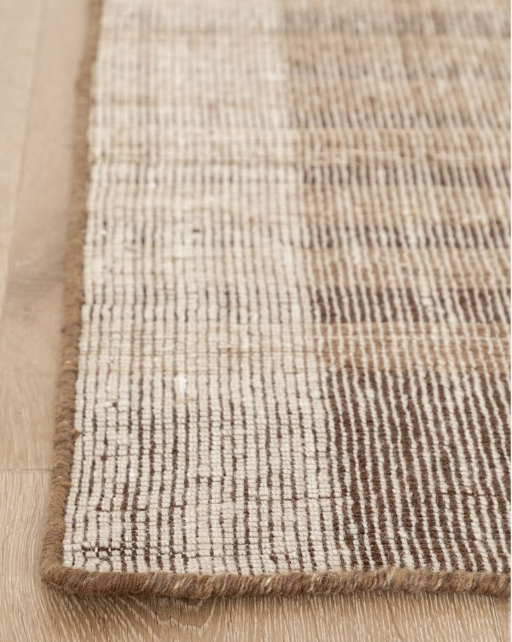 an area rug with brown and white stripes on the bottom, in front of a wooden floor