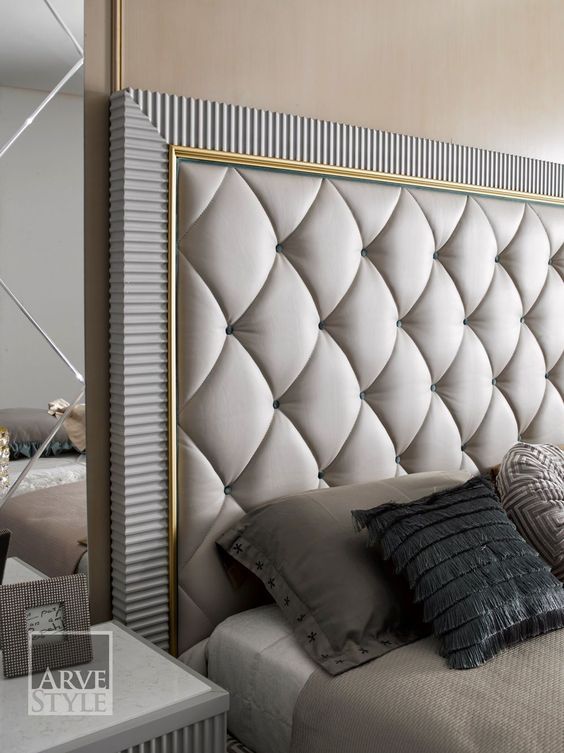 a large white bed sitting next to a mirror in a room with gold trim on the headboard