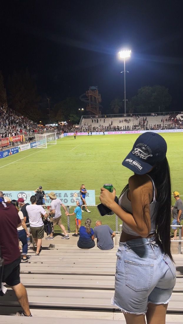 a woman standing on the bleachers in front of a baseball field at night